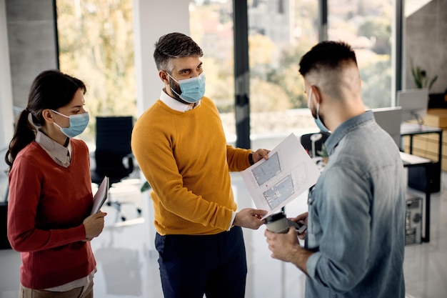 Grupo de arquitetos usando máscaras faciais enquanto analisam plantas no escritório