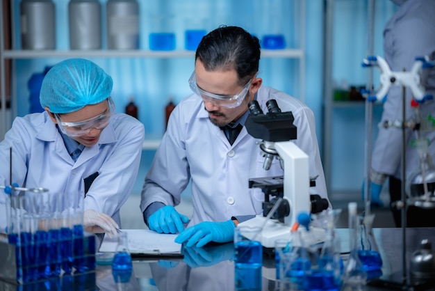 Grupo de assistentes de laboratório verificando sangue, usando microscópio e fazendo teste para bactérias