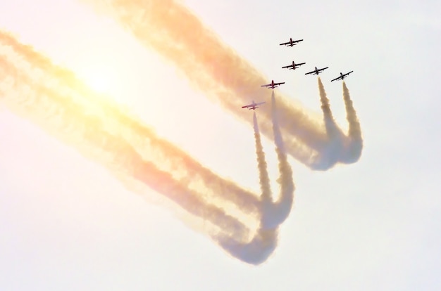 Grupo de avião a jato de combate com um traço de fumaça branca contra um céu azul.