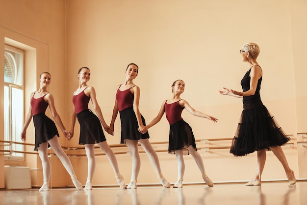 Grupo de bailarinas felizes de mãos dadas enquanto tem aula de balé com seu professor no estúdio de dança