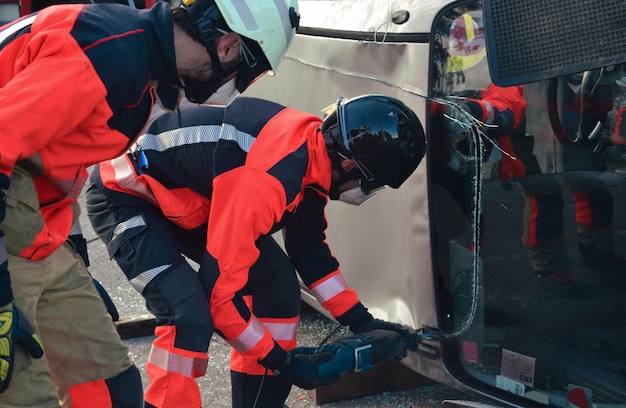 Grupo de bombeiros vestindo uniformes e capacetes realizam um resgate em um acidente de carro