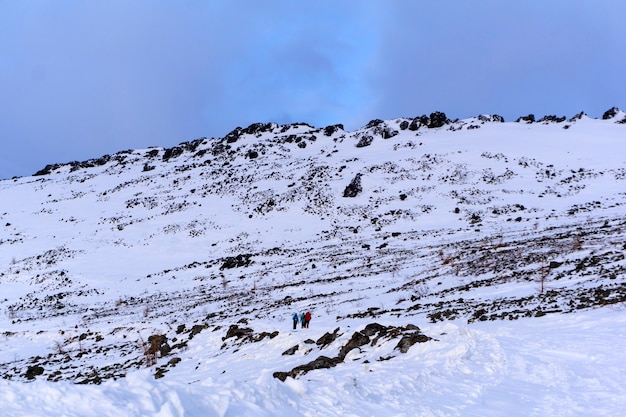 Grupo de caminhantes em uma estrada de montanha coberta de neve, cruzando uma encosta rochosa sem árvores