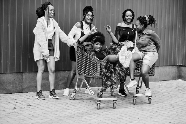 Grupo de cinco mulheres afro-americanas com carrinhos de compras se divertindo juntos ao ar livre