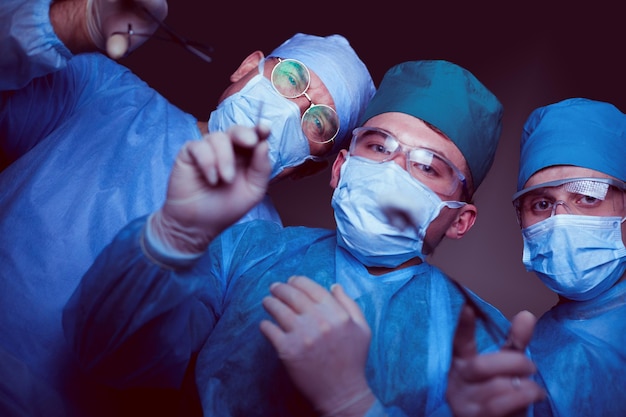 Grupo de cirurgiões no trabalho em sala de cirurgia em tons de azul. Equipe médica realizando operação