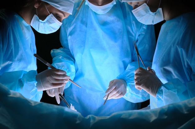 Grupo de cirurgiões no trabalho em sala de cirurgia em tons de azul. Equipe médica realizando operação