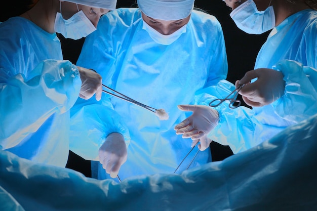 Grupo de cirurgiões no trabalho em sala de cirurgia em tons de azul. Equipe médica realizando operação