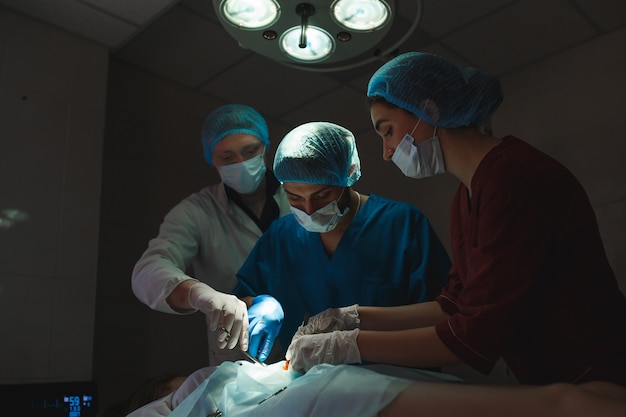Grupo de cirurgiões no trabalho operando no teatro cirúrgico. Equipe de medicina de ressuscitação usando máscaras protetoras segurando ferramentas médicas de aço, salvando o paciente. Cirurgia e emergência.