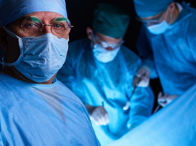 Grupo de cirurgiões trabalhando na sala de cirurgia em tons de azul Equipe médica realizando operação