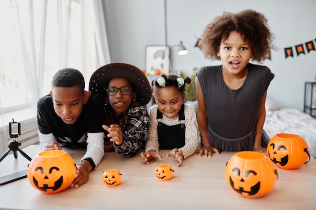 Grupo de crianças africanamerican vestidas com fantasias de halloween, posando com baldes de abóbora dentro de casa e ...