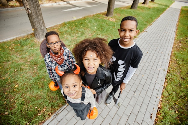 Grupo de crianças afro-americanas sorridentes, travessuras ou gostosuras ao ar livre e olhando para o espaço de cópia da câmera