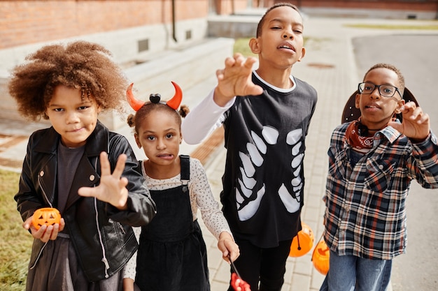 Grupo de crianças afroamericanas vestindo fantasias de halloween e posando para a câmera enquanto ...