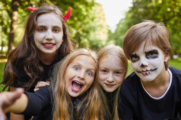 Grupo de crianças alegres em fantasias de Halloween e pintura facial enquanto tiram uma selfie ao ar livre