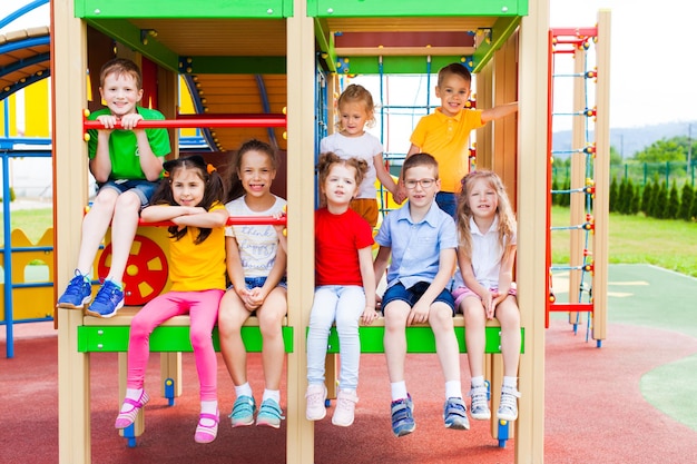 Grupo de crianças alegres sentadas na construção no parque infantil com escadas e escorregas