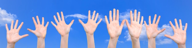 Grupo de crianças brancas caucasianas está mostrando suas mãos com palmas abertas em um fundo de céu azul em alta resolução fechada