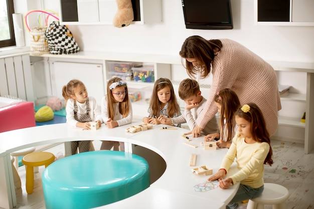 Grupo de crianças brincando com brinquedos educativos de madeira na pré-escola com a professora do jardim de infância