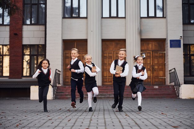 Grupo de crianças com uniforme escolar que corre juntos ao ar livre.