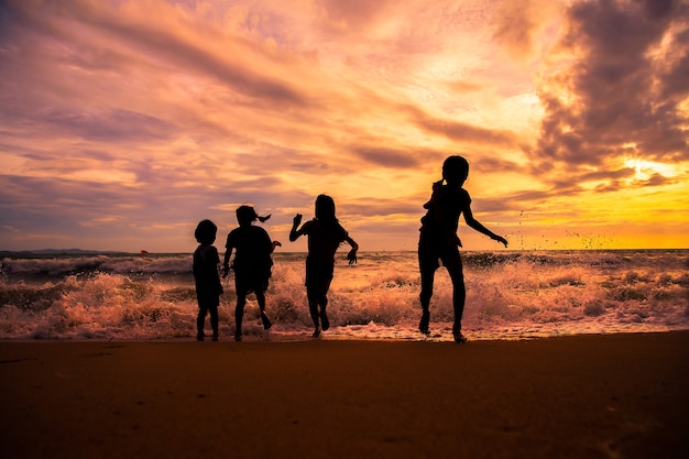 Grupo de crianças de silhueta gosta de jogar ondas do mar na praia no pôr do sol com lindo céu crepuscular