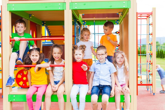 Grupo de crianças em dia de verão brincando no playground. crianças estão sentadas e sorrindo ao ar livre
