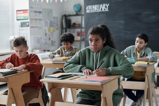 Grupo de crianças em idade escolar sentadas em suas mesas e estudando na sala de aula da escola