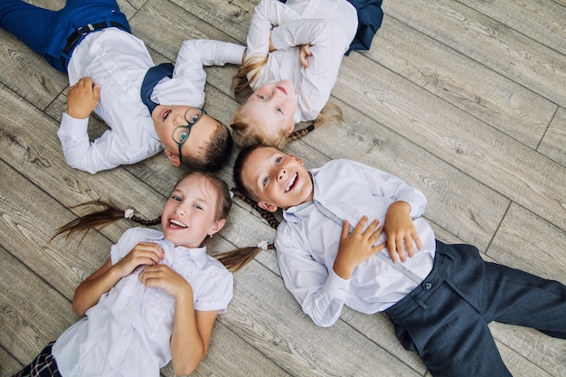 Grupo de crianças em uniforme escolar alegre e lindo sorriso deitado no chão