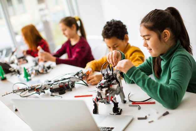 Grupo de crianças felizes programando brinquedos elétricos e robôs na sala de aula de robótica