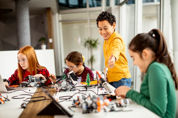 Grupo de crianças felizes programando brinquedos elétricos e robôs na sala de aula de robótica