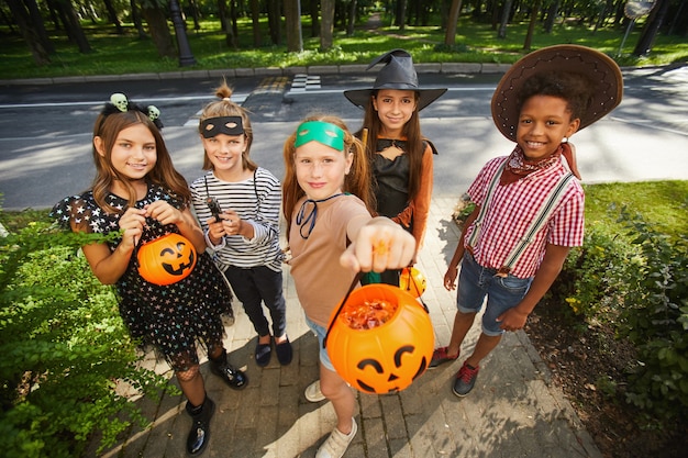 Grupo de crianças segurando cestas e pedindo guloseimas durante o feriado de Halloween ao ar livre