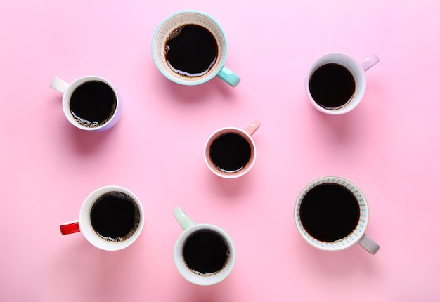 Grupo de diferentes xícaras de café no fundo rosa.