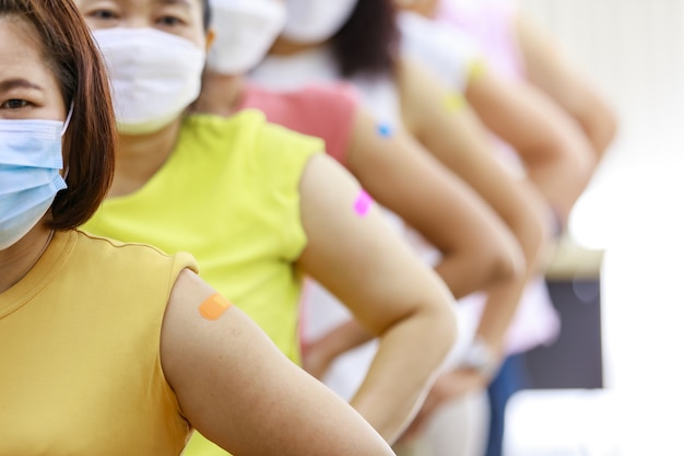 Grupo de diversas mulheres stnad em linha de linha mostram seu gesso colorido no ombro juntos após a vacinação no fundo desfocado.