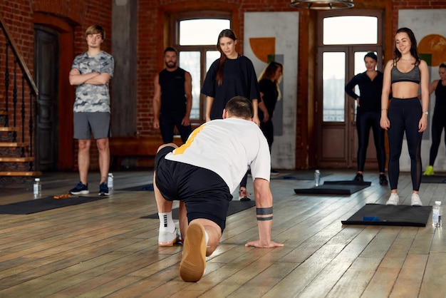 Grupo de diversos jovens em roupas esportivas fazendo exercícios de alongamento juntos na academia