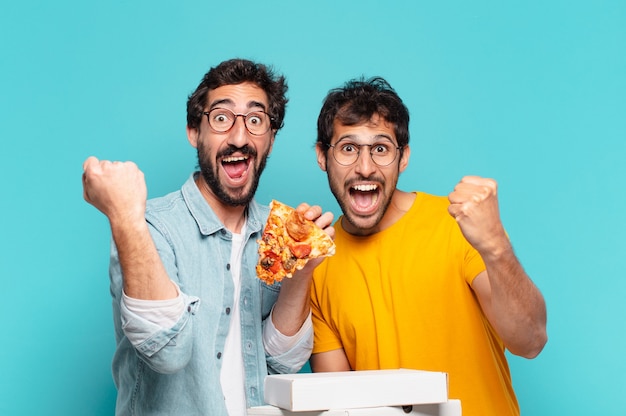 Grupo de dois amigos hispânicos comemorando uma vitória bem-sucedida e segurando pizzas para levar
