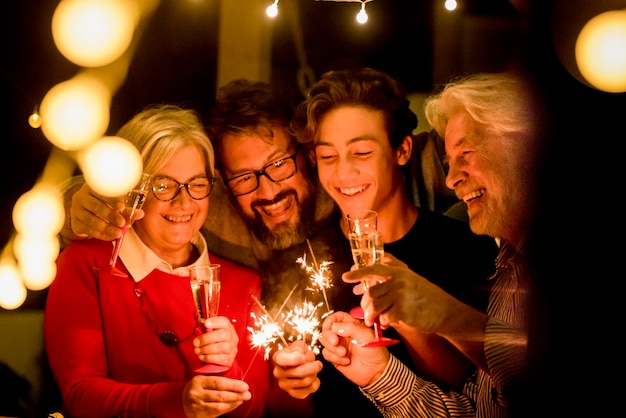 Grupo de dois idosos e dois adultos se divertindo com os sparlers o ano novo para comemorar - família feliz com luzes - segurando uma taça de champanhe