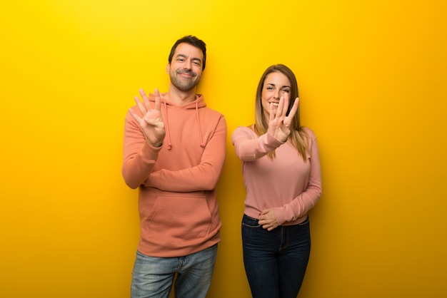 Grupo de duas pessoas no fundo amarelo feliz e contando com quatro dedos