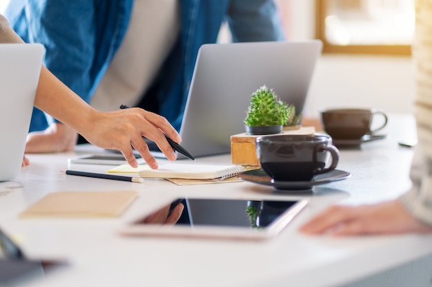 Grupo de empresário usando laptop enquanto discute e escreve no caderno sobre a mesa do escritório