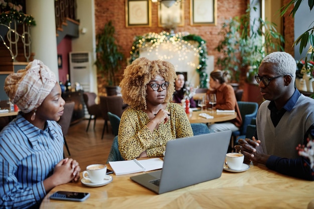 Grupo de empresários africanos sentado à mesa com o laptop, bebendo café e discutindo durante uma reunião no café