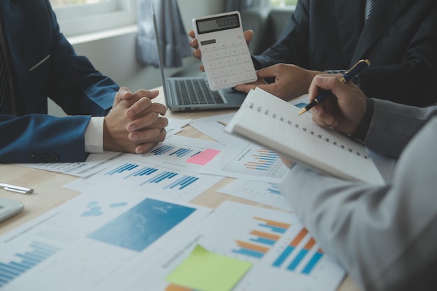 Grupo de empresários confiantes apontam para gráficos e tabelas para analisar o lucro líquido da conta de balanço de dados de mercado para planejar novas estratégias de vendas para aumentar a capacidade de produção