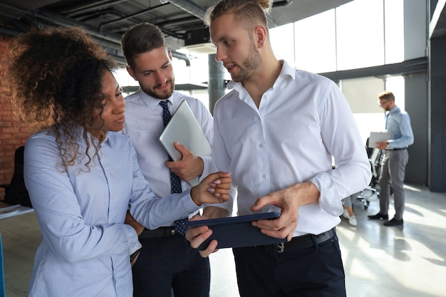 Grupo de empresários modernos está falando e sorrindo em pé no corredor do escritório.