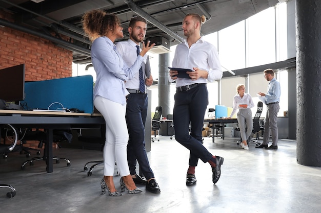 Grupo de empresários modernos está falando e sorrindo em pé no corredor do escritório.