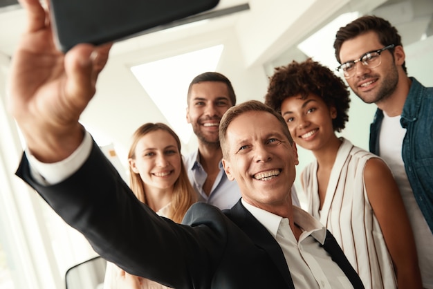 Foto grupo de equipe bem-sucedida de colegas sorridentes tirando uma selfie em um escritório moderno