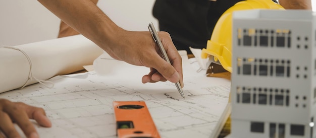 Grupo de equipe de trabalhadores da construção de arquiteto engenheiro reunindo-se na planta e modelo de construção na mesa do local de trabalho no escritório da sala de reuniões no conceito de construção do contratante do canteiro de obras