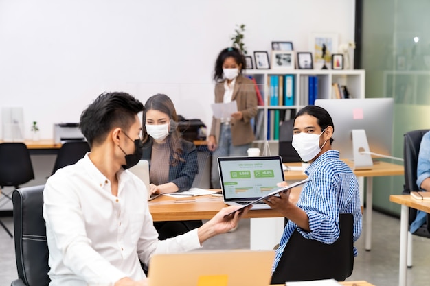 Grupo de equipe de trabalhadores de negócios inter-raciais usa máscara protetora no novo escritório normal com distância social