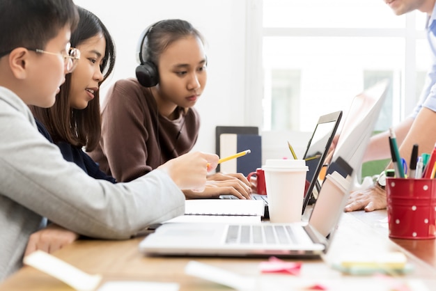 Grupo de estudantes asiáticos universitários, olhando para o computador portátil a discutir o projeto