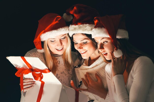 Grupo de estudantes do sexo feminino em trajes de papai noel abrindo uma caixa de presentes de natal