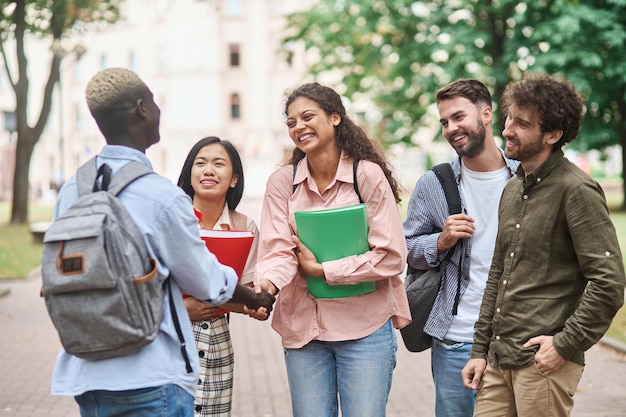 Grupo de estudantes encontrando seu amigo com um aperto de mão