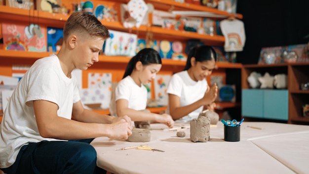 Grupo de estudantes felizes, inteligentes e diversificados trabalhando com barro na oficina Edificação