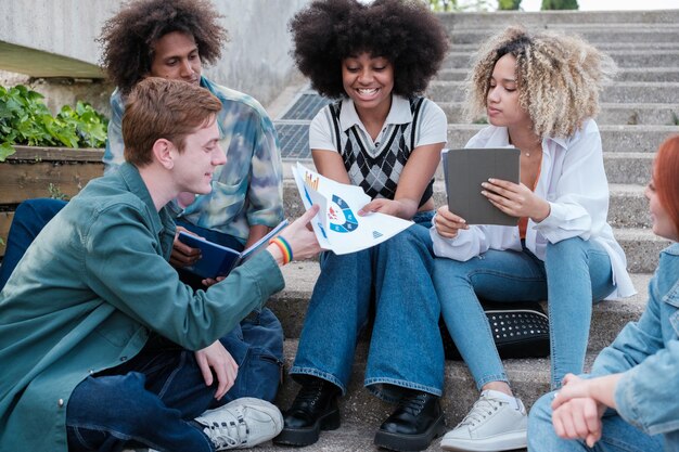 Grupo de estudantes sentados ao ar livre compartilhando gráficos sobre os estudos conceito de estilo de vida estudos carreira universitária