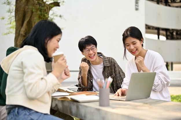 Grupo de estudantes universitários asiáticos alegres comemorando juntos o sucesso do projeto