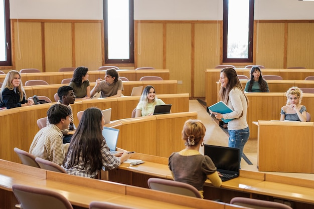 Grupo de estudantes universitários em uma sala de aula circular com o professor no meio explicando