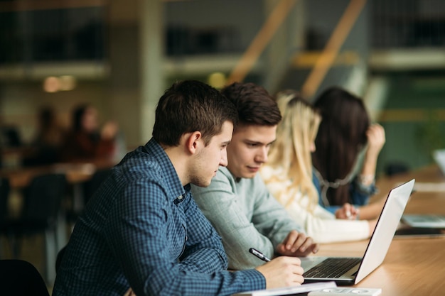 Grupo de estudantes universitários estudando na biblioteca da escola uma menina e um menino estão usando um laptop e se conectando à internet