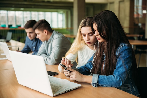 Grupo de estudantes universitários que estudam na biblioteca da escola, uma menina e um menino estão usando um laptop e